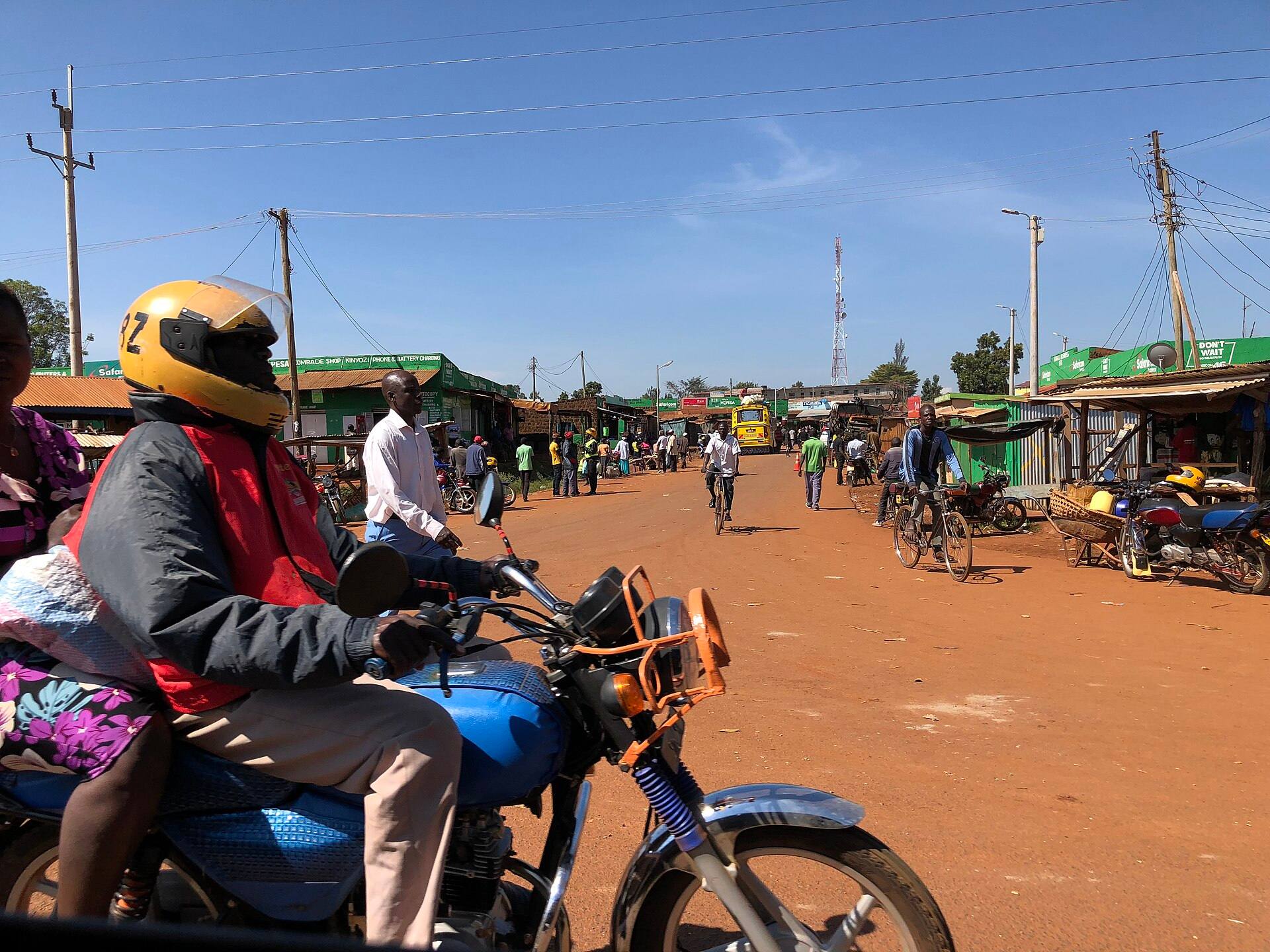A boda-boda rider on a red dirt road in Busia town, with shops and people behind