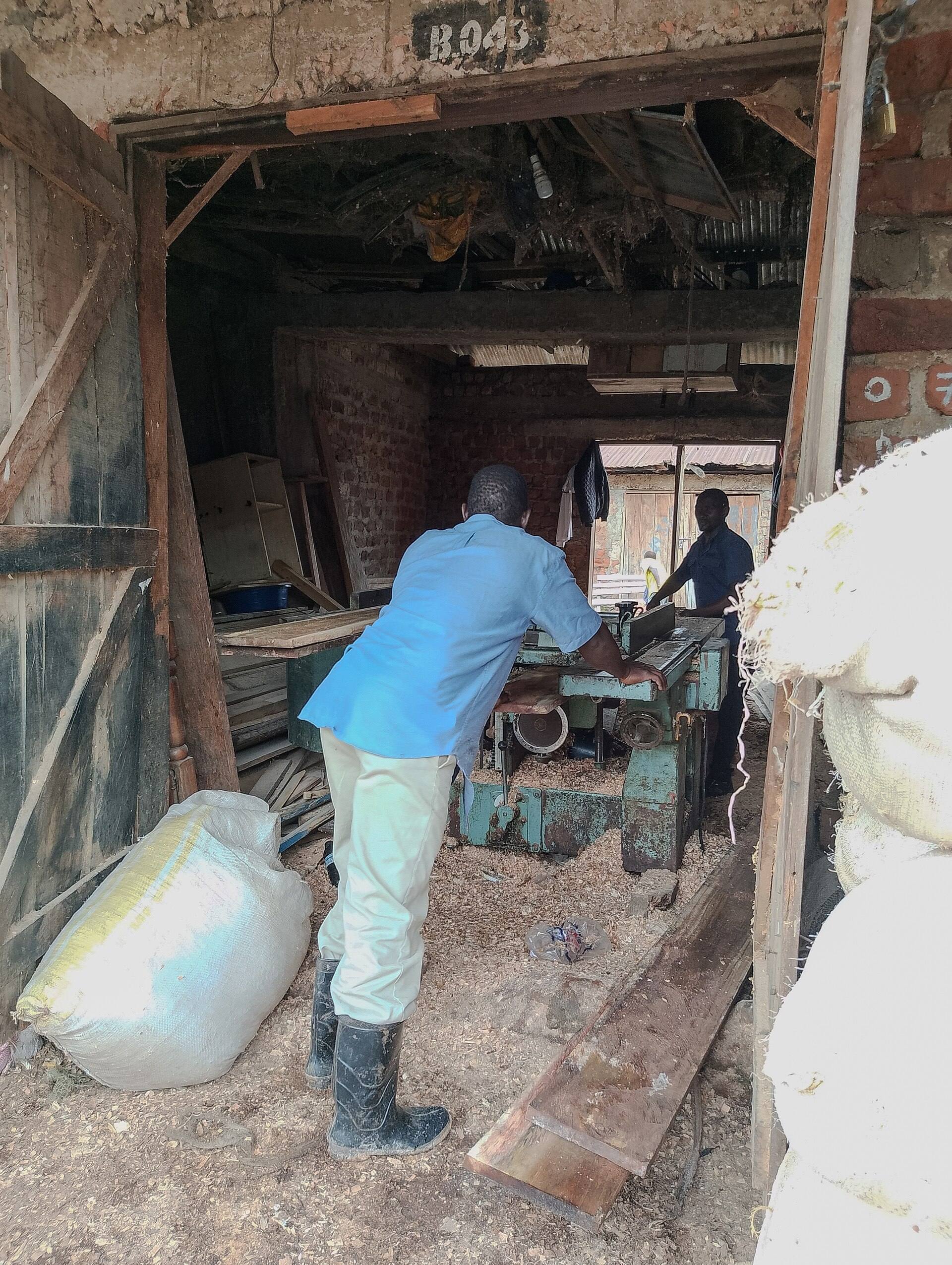 Two carpenters working with timber in an open workshop at Ggaba Landing Site